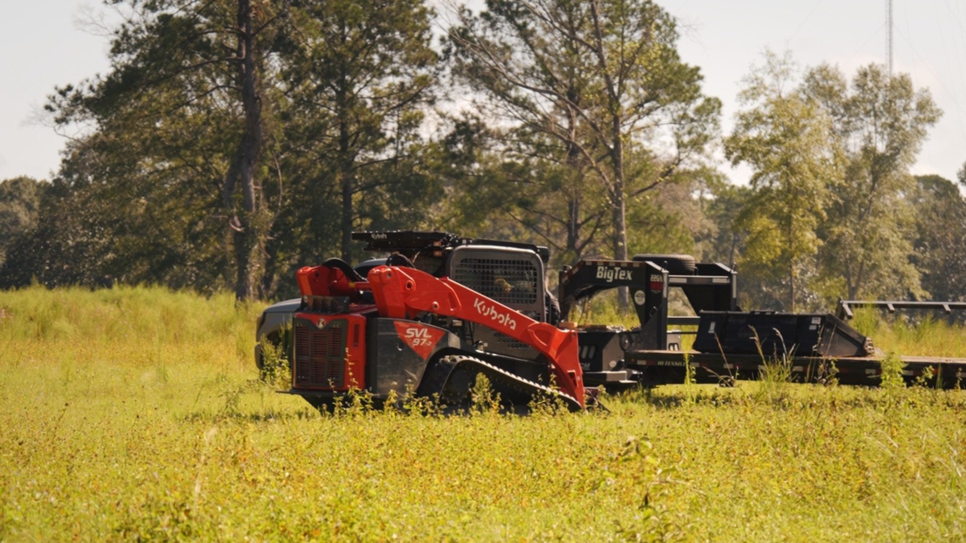 Bayou State forestry mulcher clearing tall brush on a Louisiana job site, with a dump trailer and roll-off bin parked at the treeline